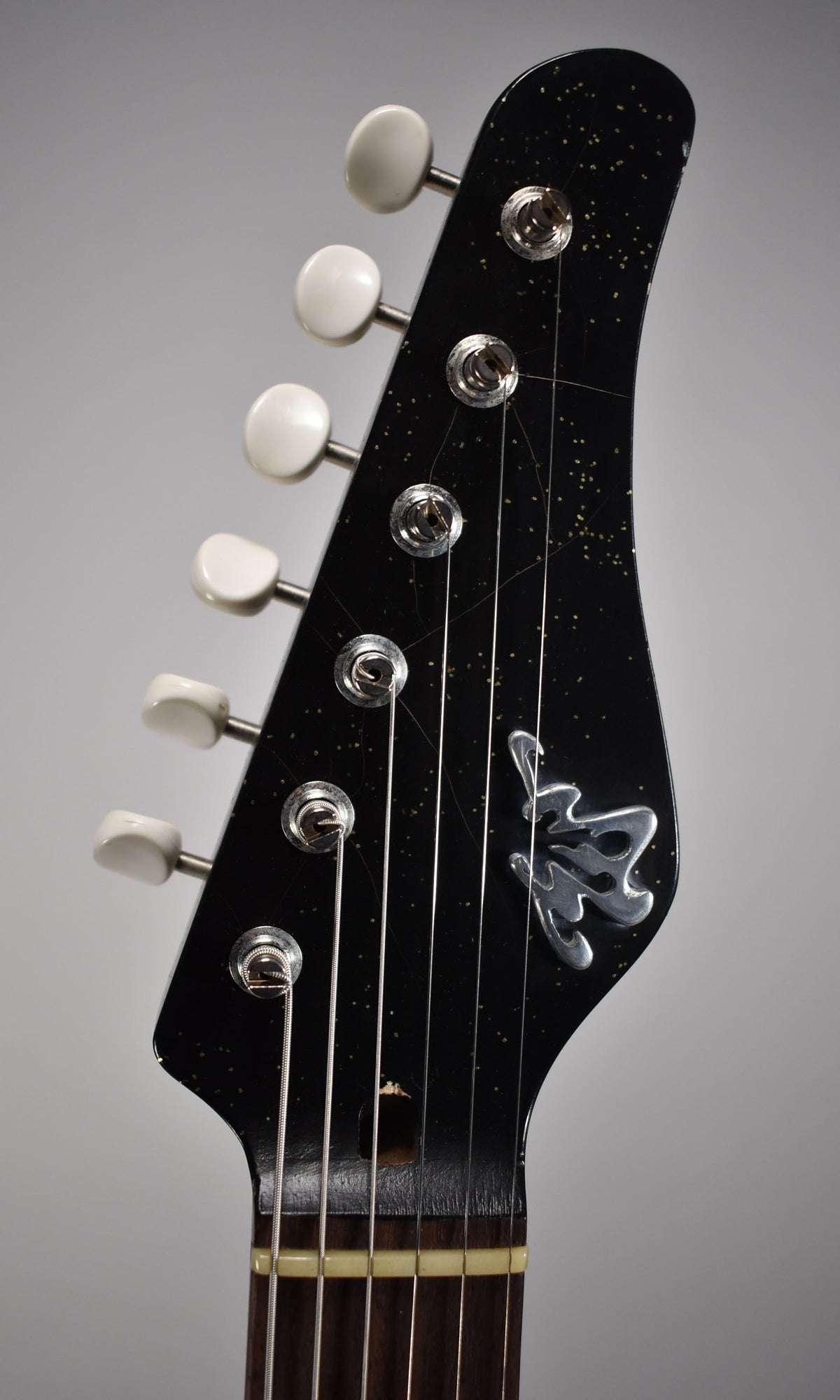 Close-up of the black sparkle headstock with white tuners, showing a silver logo, light wear, and a visible truss rod access.
