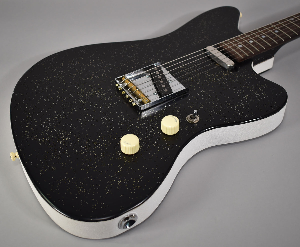 Close-up of a black sparkle electric guitar with white binding, two cream control knobs, a toggle switch, and a chrome bridge.