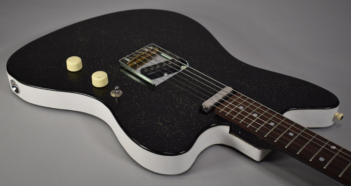 Black sparkle electric guitar, angled from above, showing the body's white textured sides, two cream knobs, and a single chrome pickup.