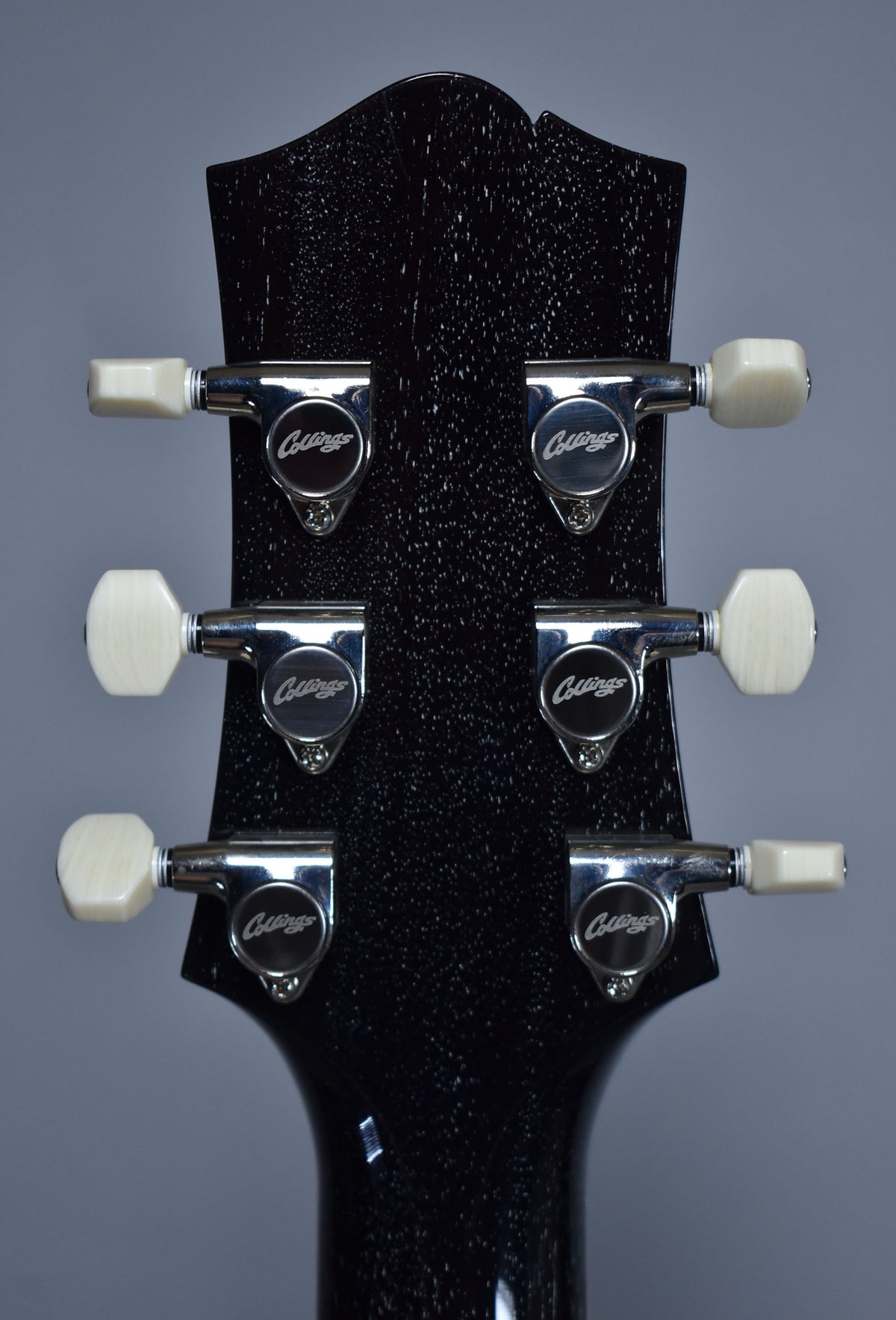 Rear view of the guitar's black doghair headstock with six chrome tuners, each featuring an off-white octagonal button.