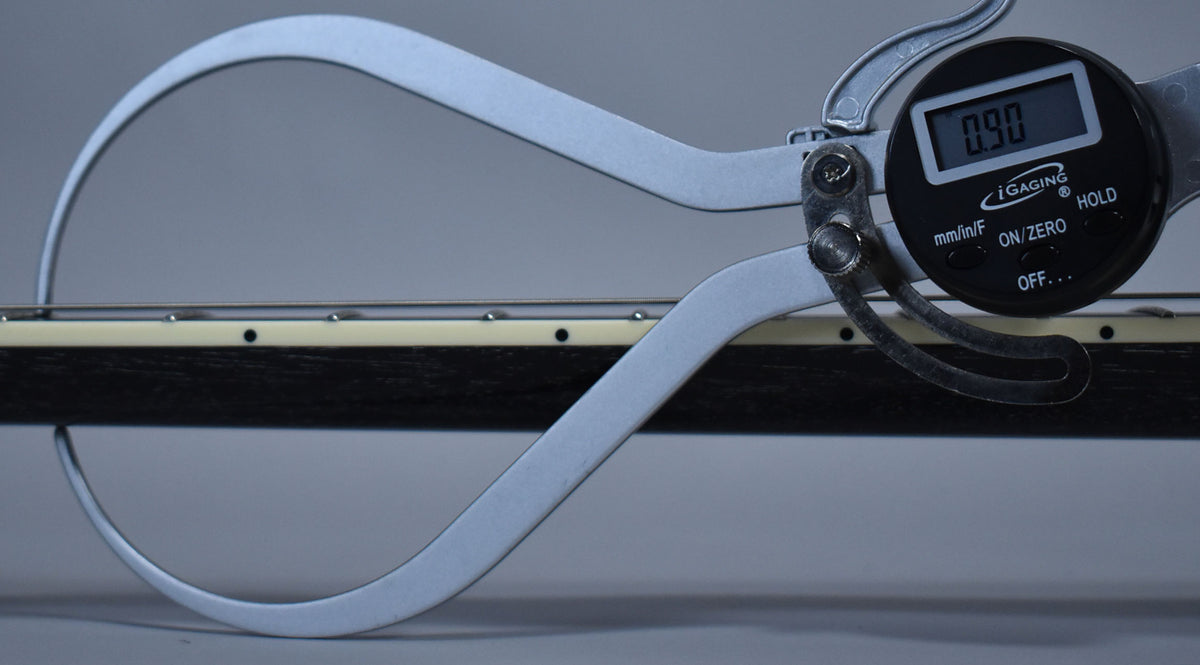 A digital caliper measures the guitar's dark fretboard with cream binding, showing a reading of 0.90.