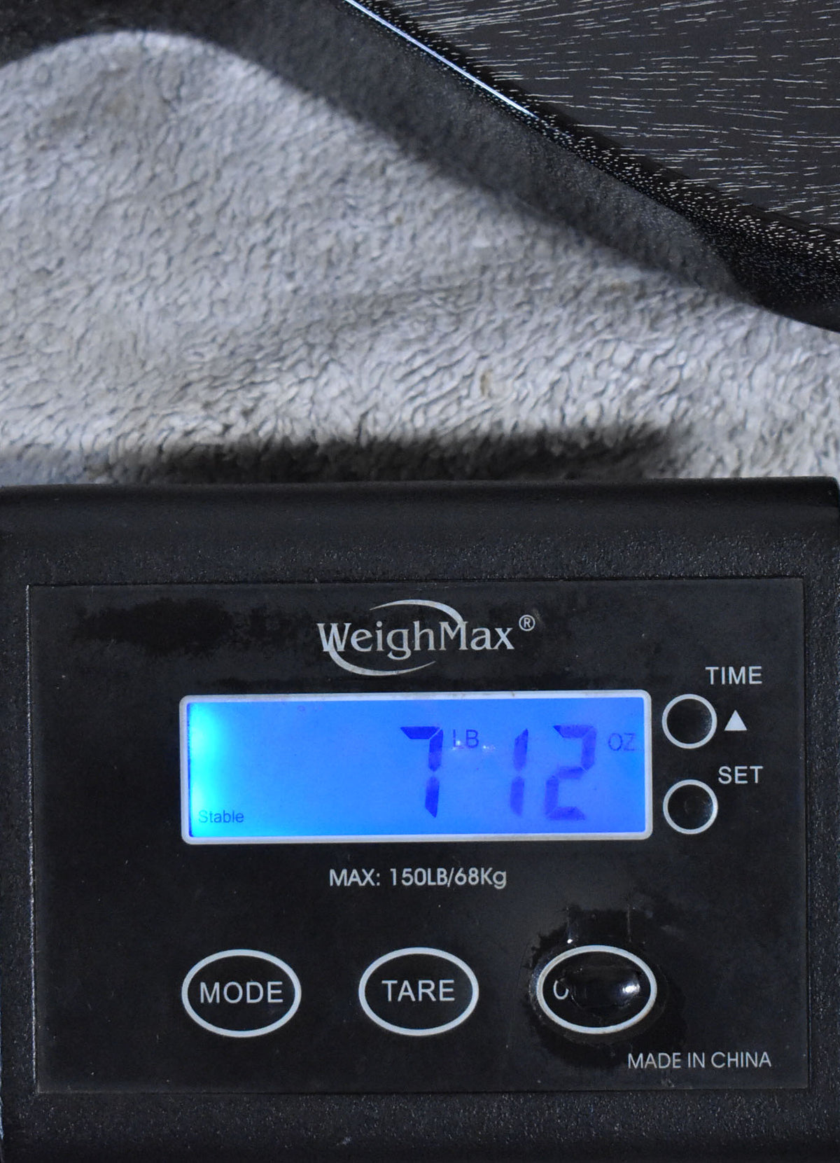 A black digital scale displays "7 LB. 12 OZ." with a portion of the guitar's black doghair finish visible above.