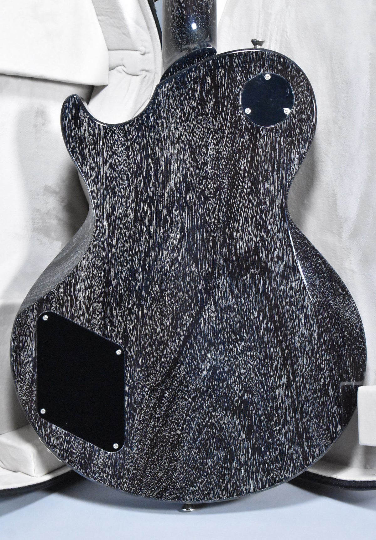 The back of a black electric guitar with a doghair finish, showing a round control cavity cover and a rectangular access plate.