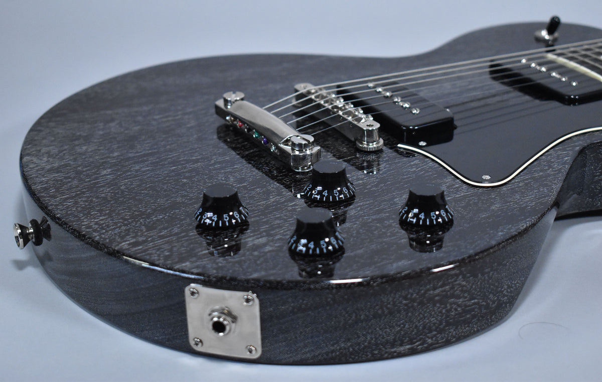 Close-up of a black doghair-finished electric guitar body, showing four black control knobs, a chrome bridge, and a black pickguard.