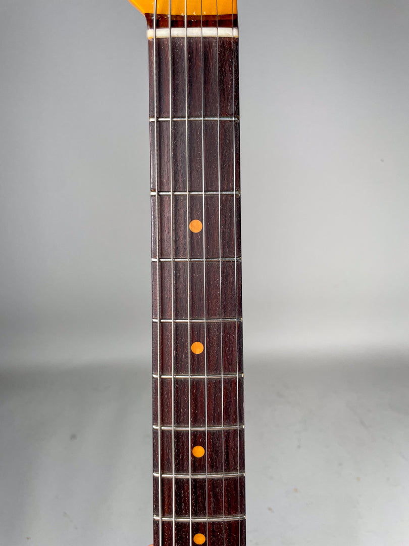 Close-up of the dark rosewood fretboard with bright orange dot inlays and shiny frets, showing light wear on the lower frets.