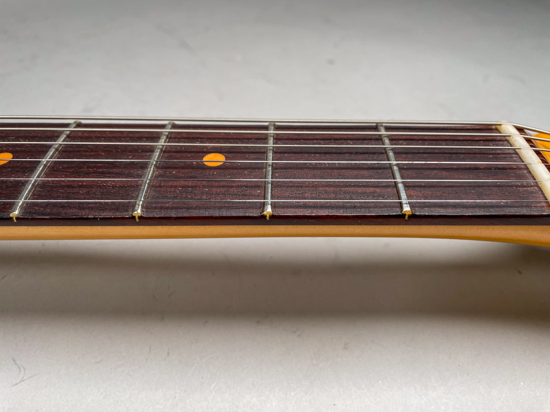 Close-up of the dark rosewood fretboard with light orange dot inlays, showing frets 1 through 7 and the light-colored nut.