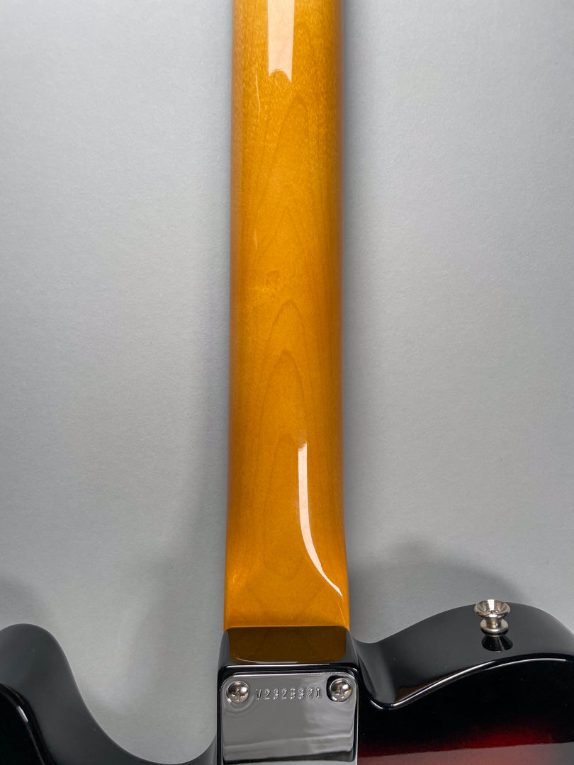 Rear view of the guitar's glossy amber neck, showing the chrome neck plate with visible serial number and a strap button.