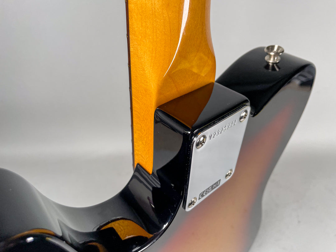 Close-up of the guitar's sunburst body and glossy neck heel, with a chrome neck plate showing a serial number and four screws.