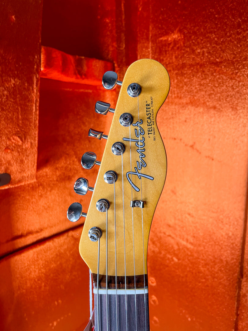 Close-up of the guitar's headstock, showing the light amber finish, six chrome tuners, and string tree, against an orange case lining.