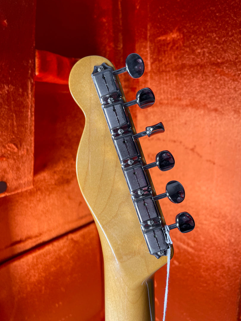 Close-up of the guitar's headstock and neck heel, showing the light blonde finish, chrome tuners, and a white tag.