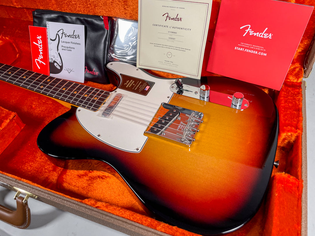 Sunburst Telecaster in a brown hard case with orange plush lining, showing the body, neck, and case candy from above.