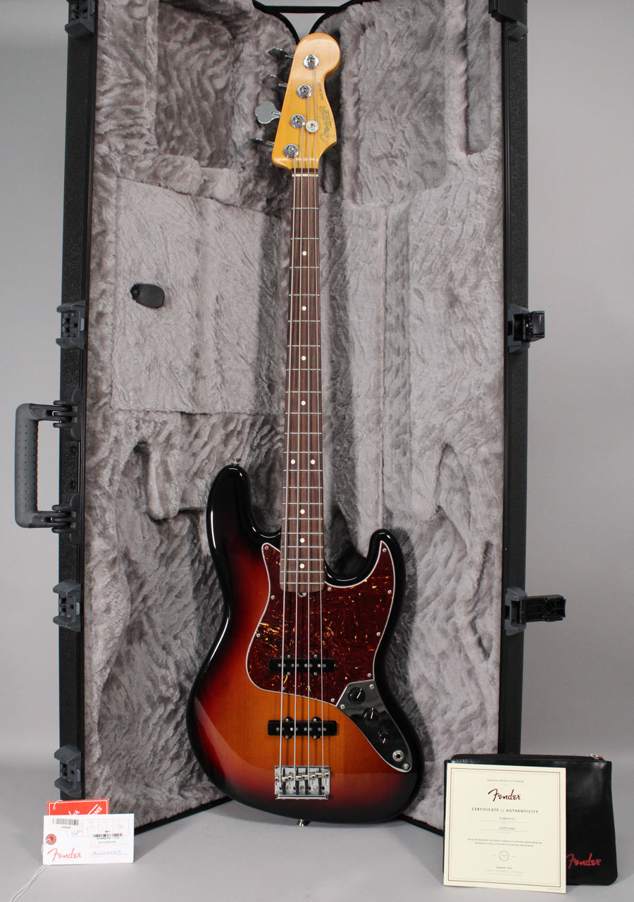 Full-length view of a glossy 3-color sunburst bass with a tortoiseshell pickguard, resting in a plush gray hard case.
