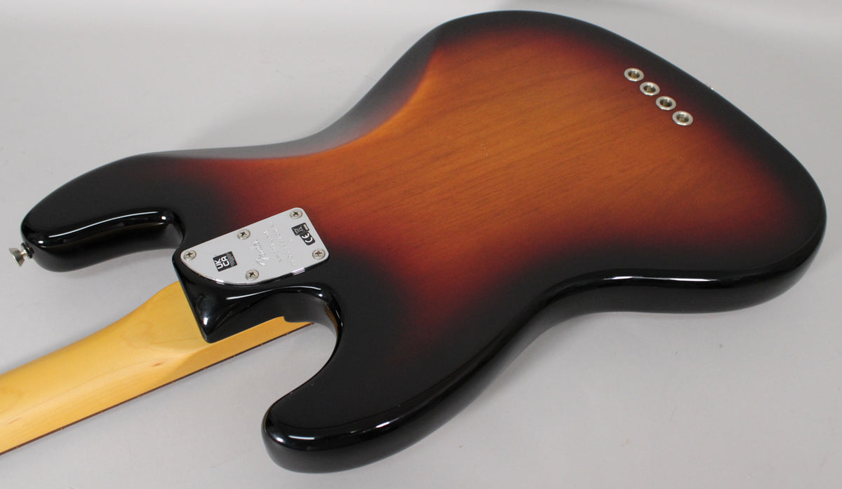 The bass guitar's glossy 3-color sunburst body is viewed from the back, showing the chrome neck plate and four string ferrules.