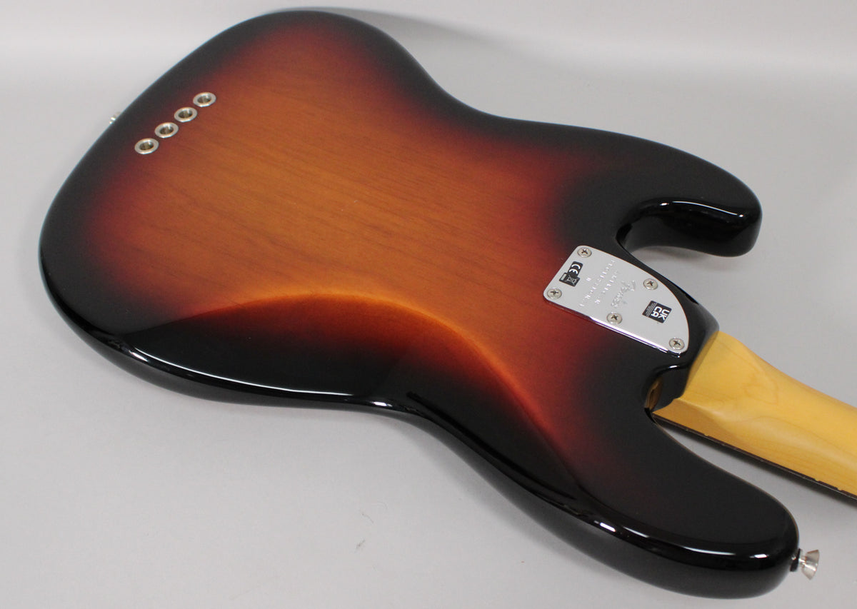 The back of a sunburst bass guitar, angled to show the body's glossy finish, chrome neck plate, and four string ferrules.