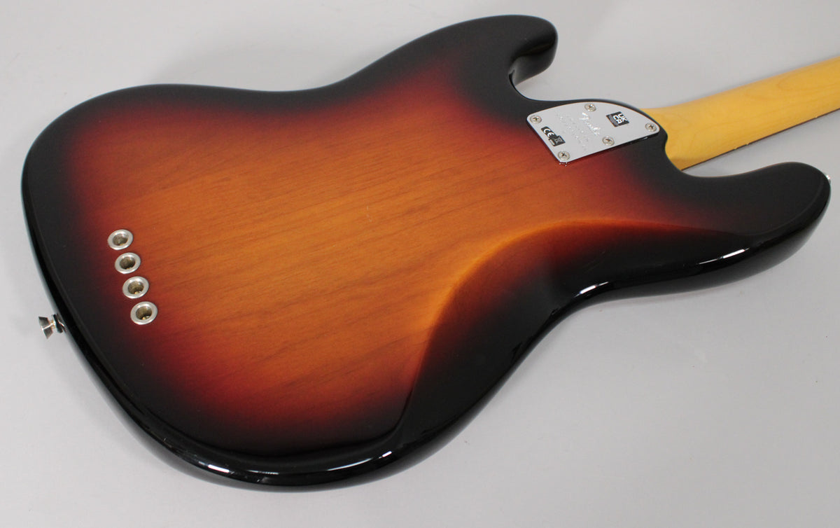 The bass guitar's glossy 3-color sunburst body is viewed from the back, angled to show the neck plate and string-through-body ferrules.