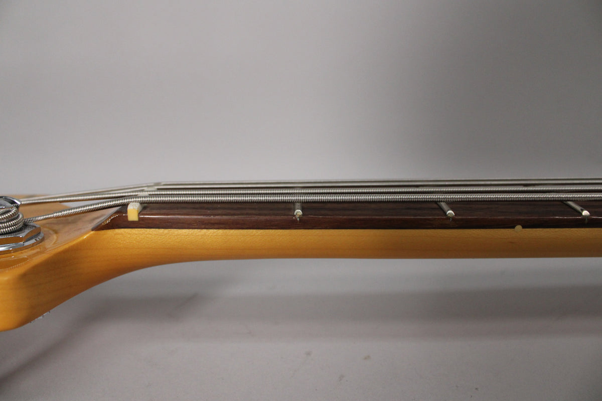 Close-up of the bass neck from the side, showing the light maple neck, dark rosewood fretboard, and four strings over the nut.