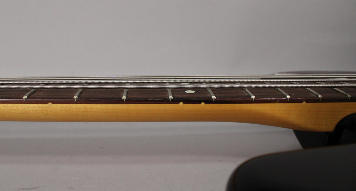 Close-up of the bass guitar's fretboard and neck, showing white dot inlays and side dots, with a light wood neck.