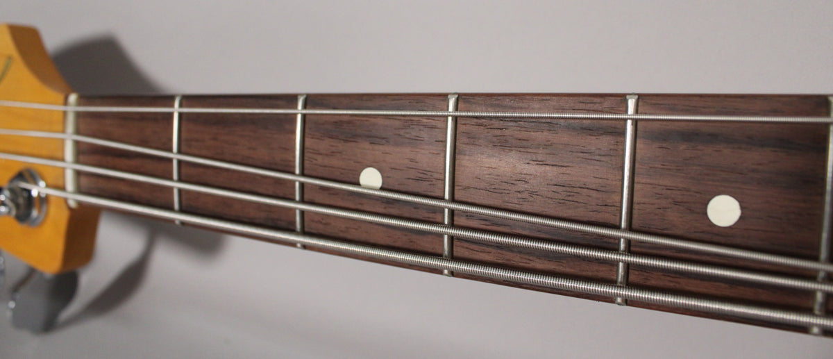 Close-up of the bass's dark wood fretboard with four strings, metal frets, and two white dot inlays.