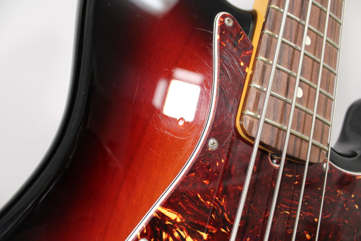 Close-up of the bass's upper body, showing a glossy 3-color sunburst finish with many light scratches and a tortoiseshell pickguard.
