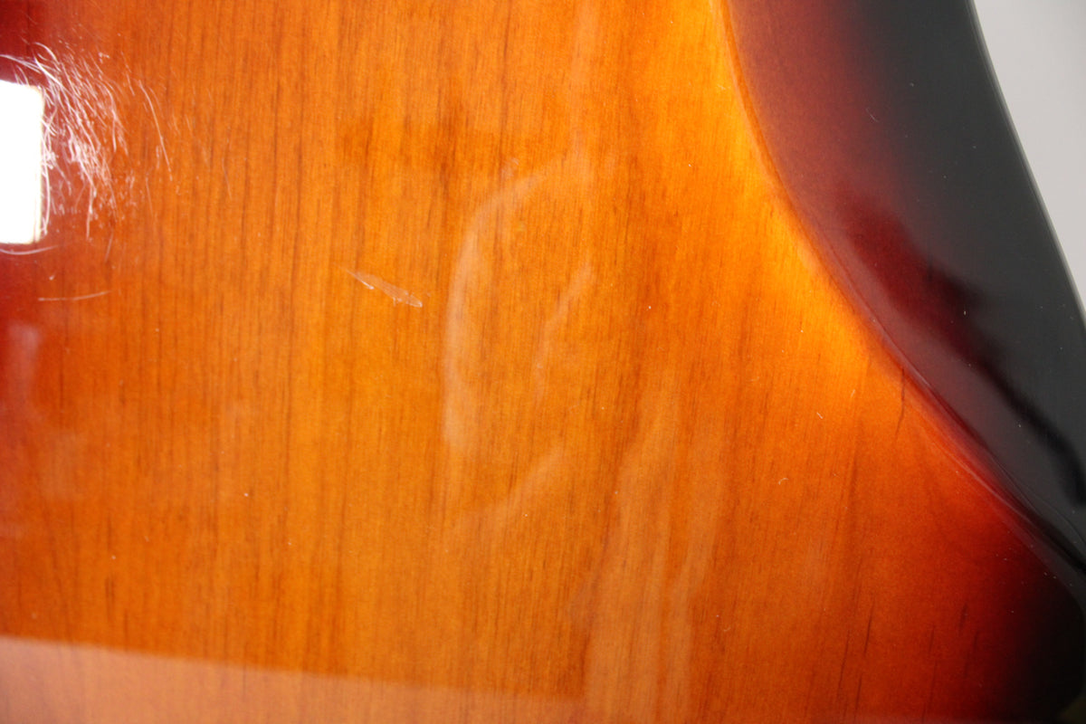 Close-up of the bass body's lower bout, showing the sunburst finish with light scratches and a few small dings on the brown and orange areas.