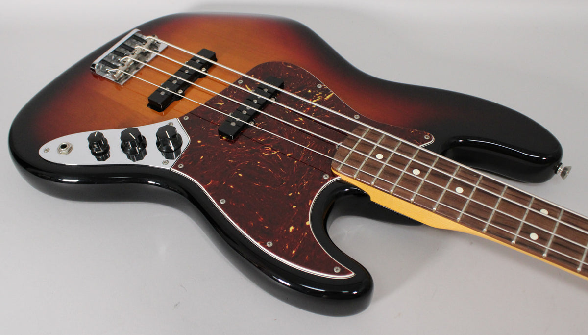 The upper body of a sunburst Jazz Bass, with a tortoiseshell pickguard, two pickups, and four chrome control knobs.