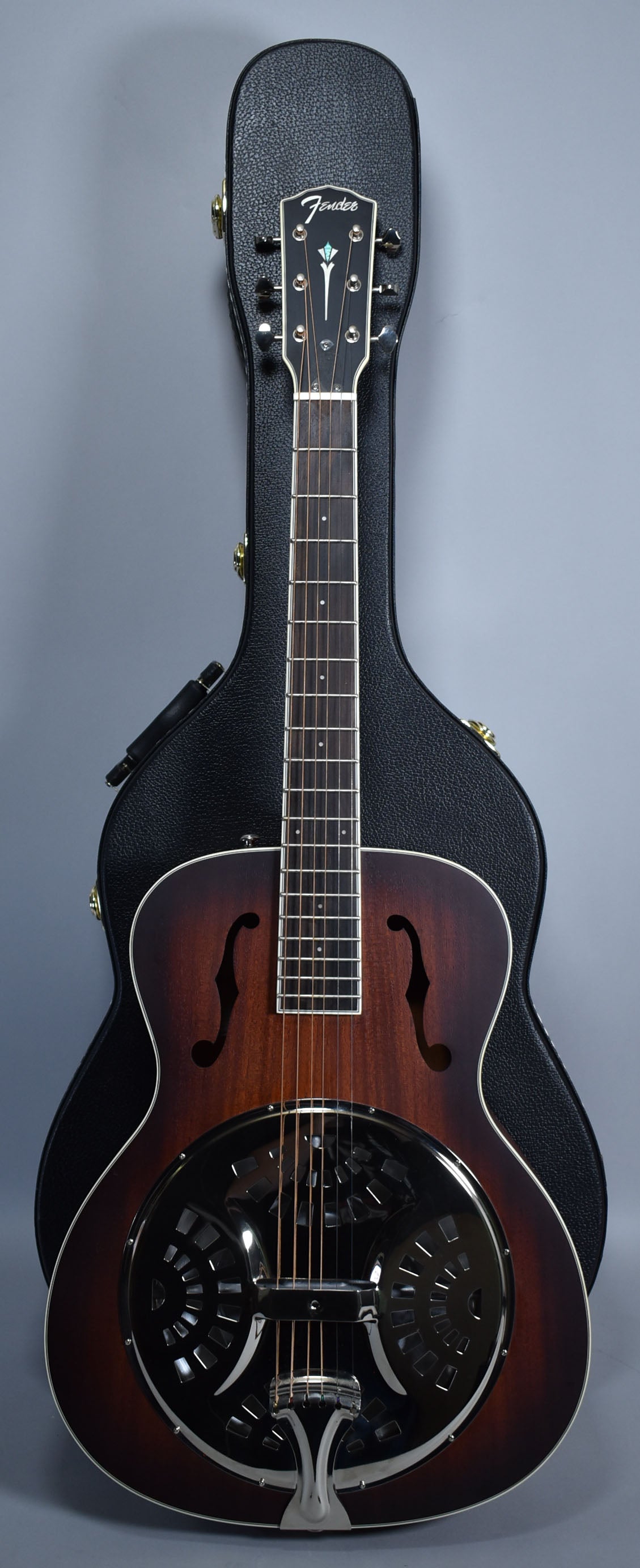 A full-length view of a dark sunburst resonator guitar with f-holes, a chrome resonator cone, and a black hard case behind it.