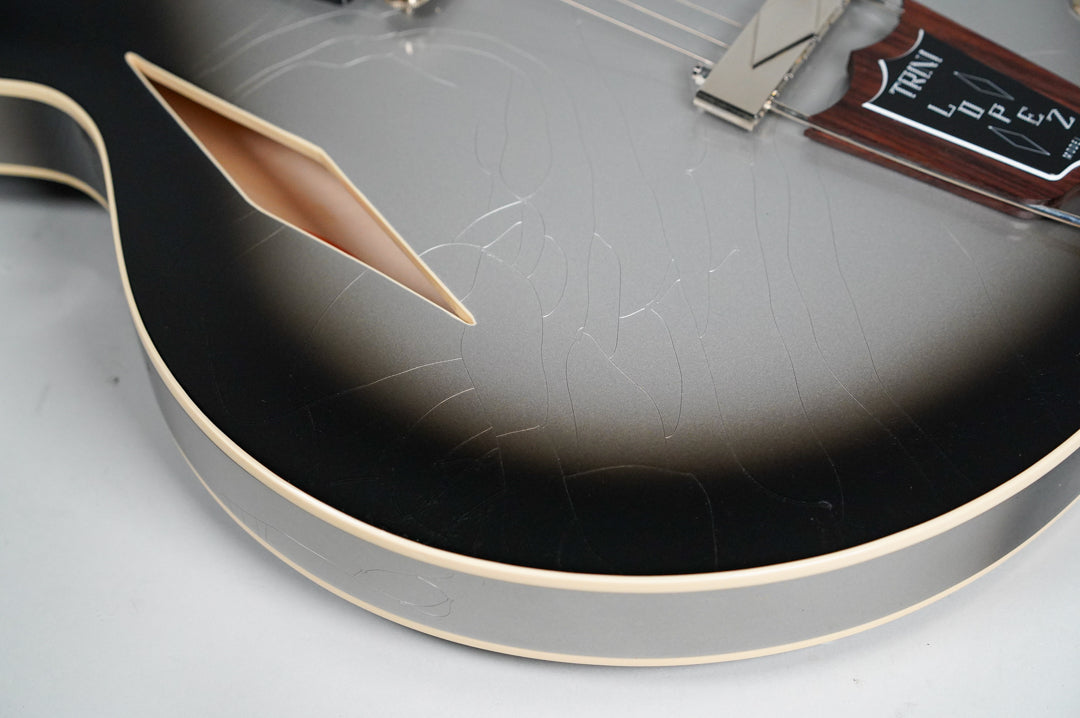 Close-up of the guitar's lower bout, showing the silverburst finish with extensive checking, a f-hole, and a dark wood tailpiece.