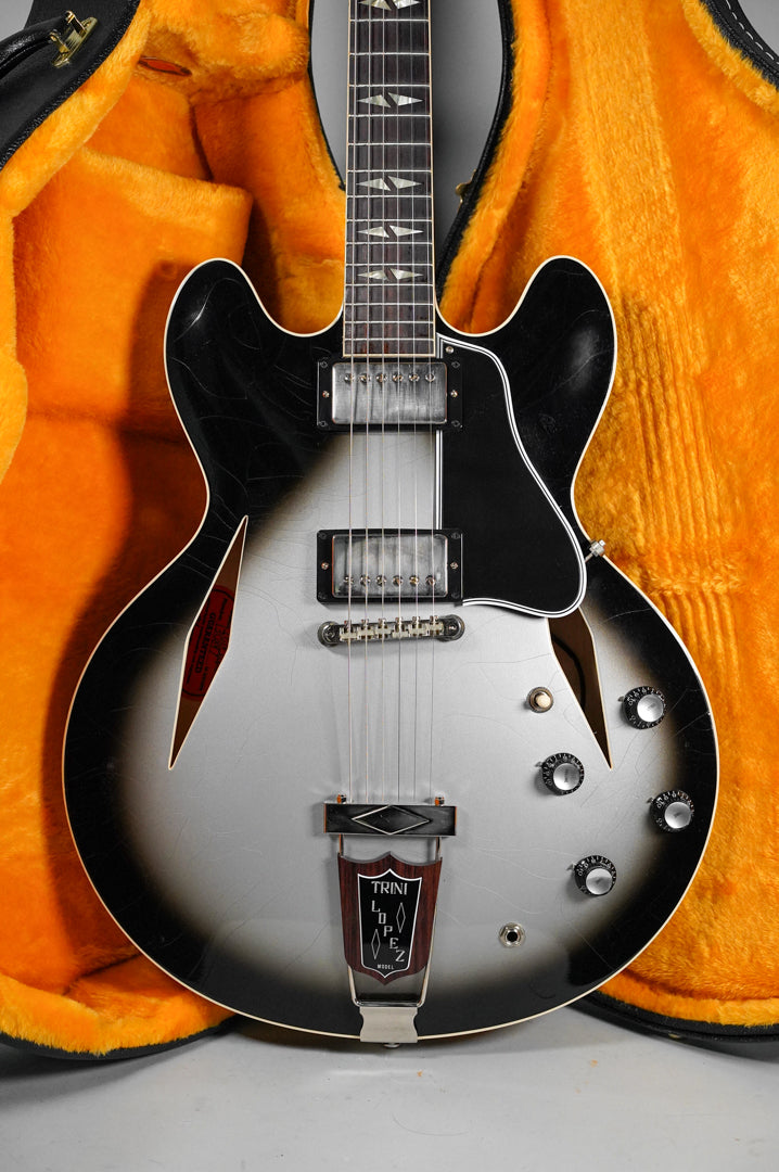 Full front view of a silverburst semi-hollow guitar with black f-holes, two humbuckers, and four black control knobs, resting in an orange-lined case.