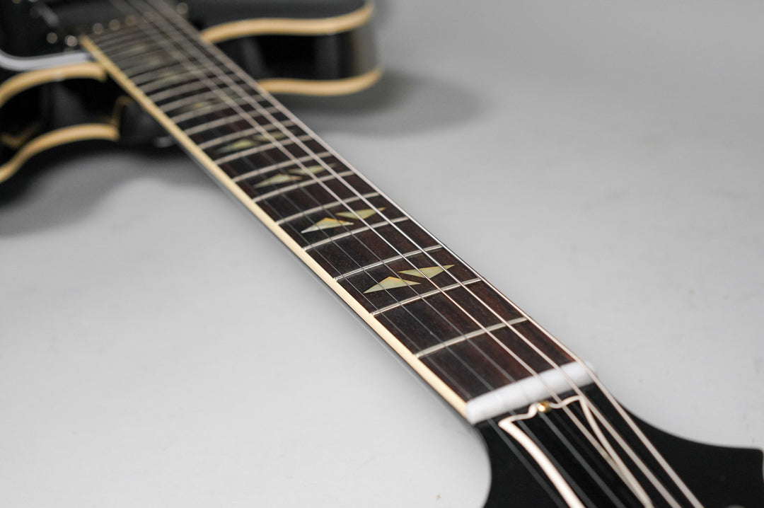 Close-up of the dark fretboard with light trapezoid inlays, showing the nut and strings leading to the black headstock.