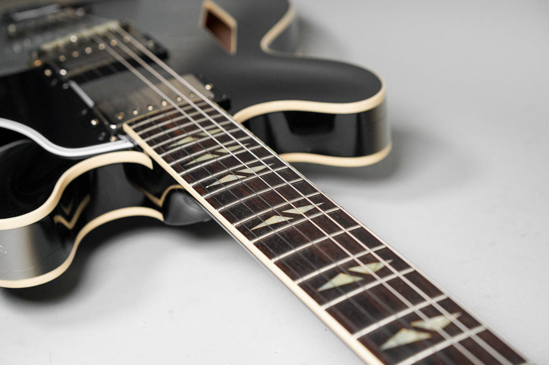 Close-up of the dark fretboard with parallelogram inlays, showing the black body with cream binding and f-hole in the background.