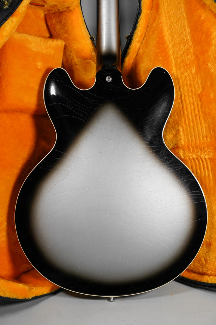 The guitar's back, a silverburst finish with extensive checking, is visible in its open orange-lined hard case.