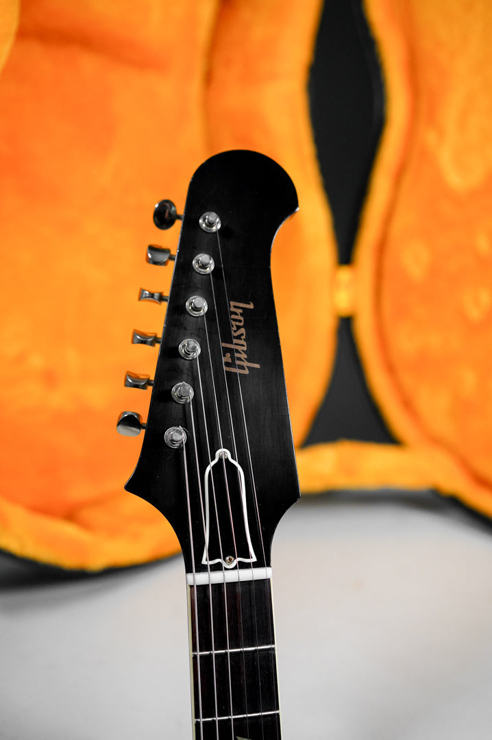 The guitar's black headstock, with six tuners and a bell-shaped truss rod cover, is angled slightly right against an orange case.