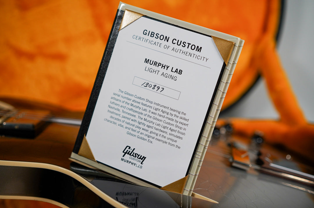 Close-up of the guitar's certificate of authenticity, with the guitar's dark body and orange case lining blurred in the background.