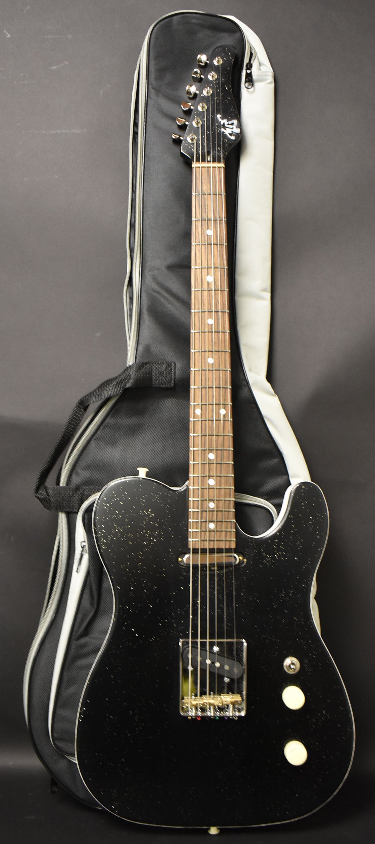 A black sparkle electric guitar with a single bridge humbucker and two cream control knobs, leaning against a black gig bag.