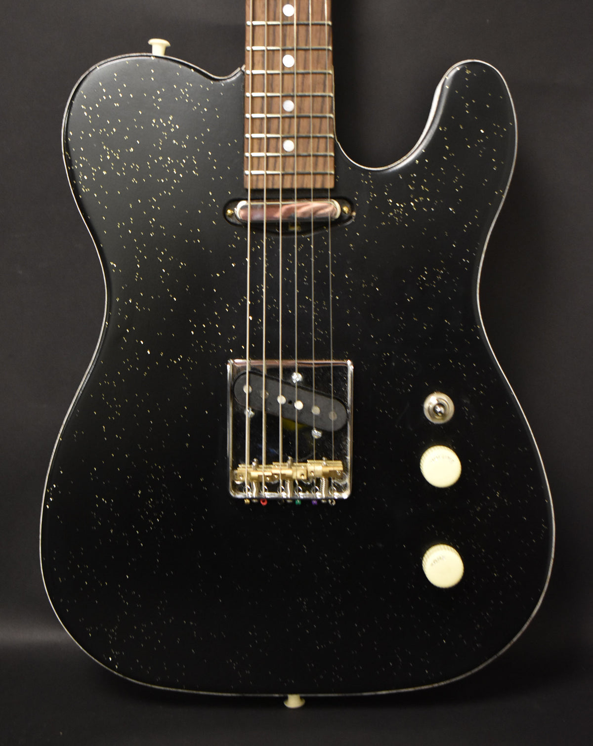 Black sparkle electric guitar, full body view, with a gold bridge, black bridge pickup, and two cream control knobs.