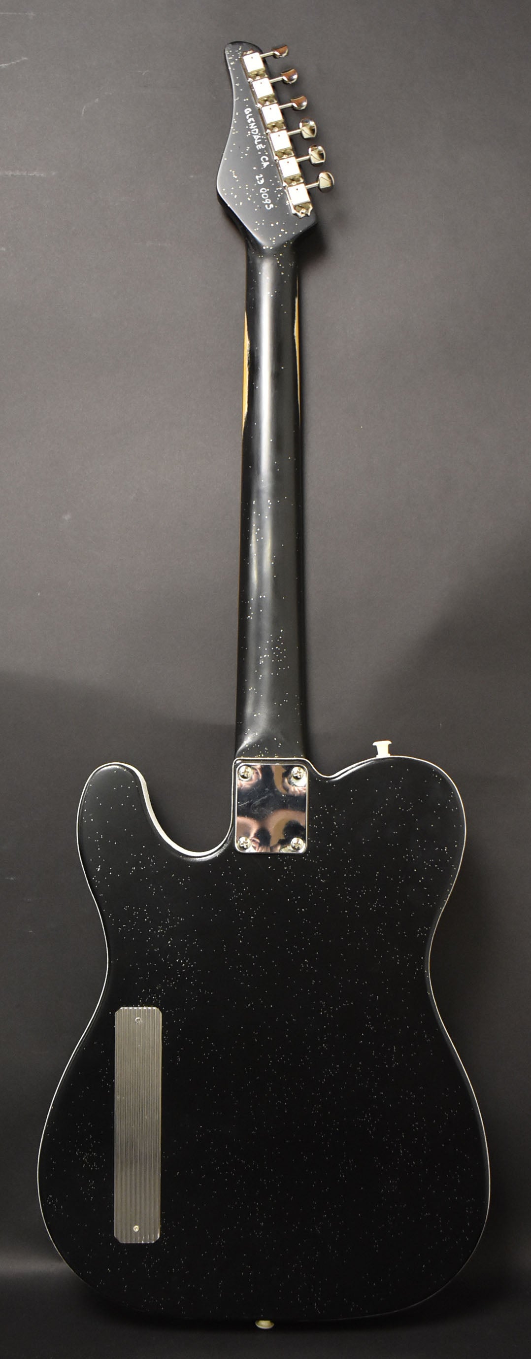 Full back view of a black sparkle electric guitar with a white binding, chrome neck plate, and a ribbed chrome control cover.