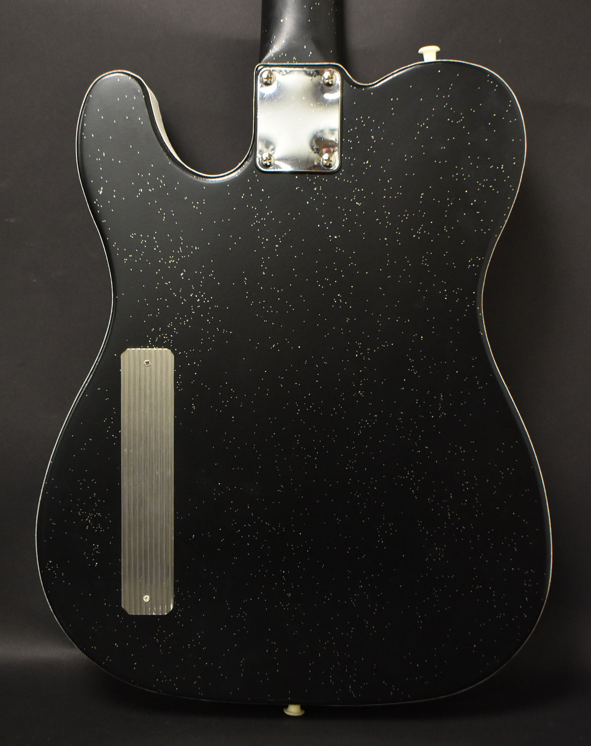 Rear view of a black sparkle electric guitar, showing the chrome neck plate and a ribbed metal control cavity cover.