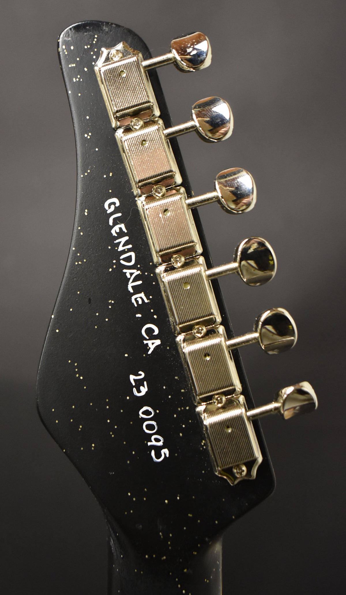 Close-up of the black sparkle headstock with six gold-plated, ribbed tuners and a slight chip on the top edge.