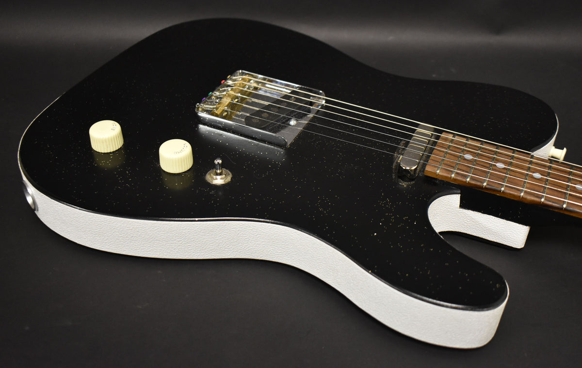The black sparkle electric guitar body, with white textured sides, features two cream control knobs, a toggle switch, and a chrome bridge.