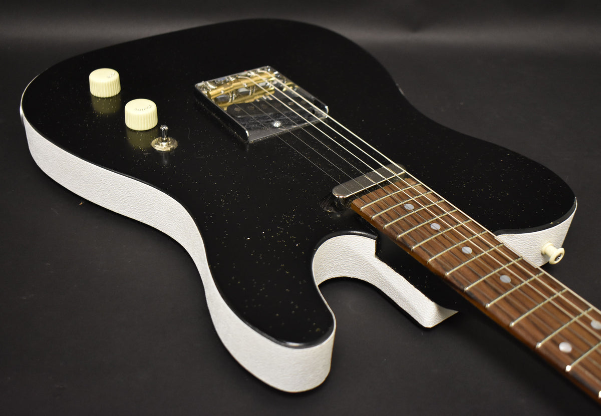 The black sparkle electric guitar body, with white textured sides, is angled from the upper left, showing two cream control knobs.