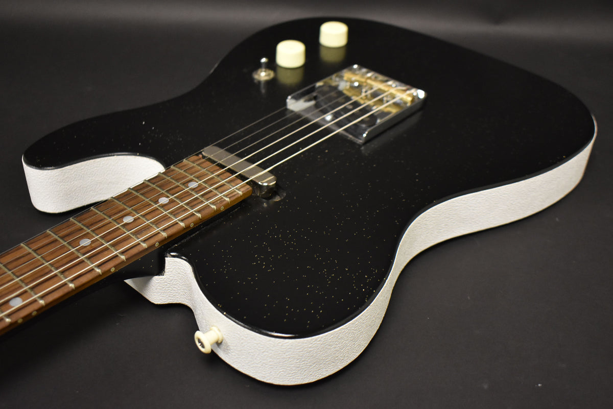 Close-up of the black sparkle guitar body with white textured sides, showing the fretboard, bridge, two cream knobs, and a toggle switch.