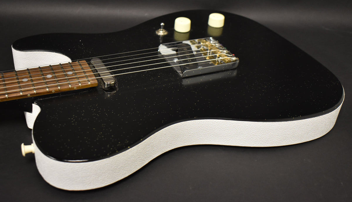 Angled view of a black sparkle guitar body with white textured sides, two cream knobs, and a chrome bridge with gold flecks.