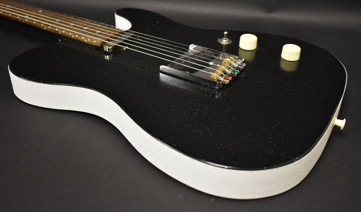 The black sparkle guitar body, with white textured sides, is angled to show the bridge, two cream control knobs, and a toggle switch.