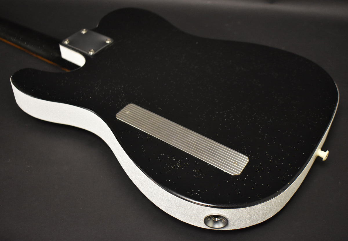 The guitar's black sparkle back and white sides are angled, showing a metal neck plate, string-through plate, and output jack.