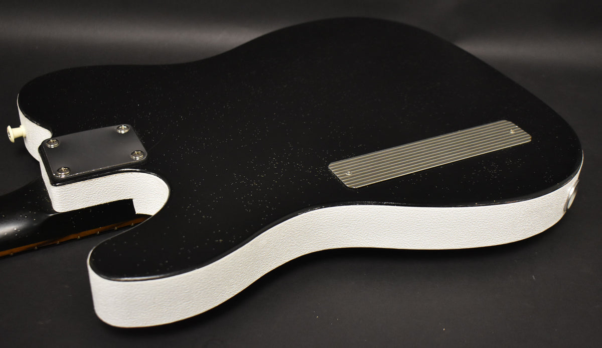 The guitar's black sparkle back and white textured sides are visible, with a metal neck plate and a ribbed control cavity cover.