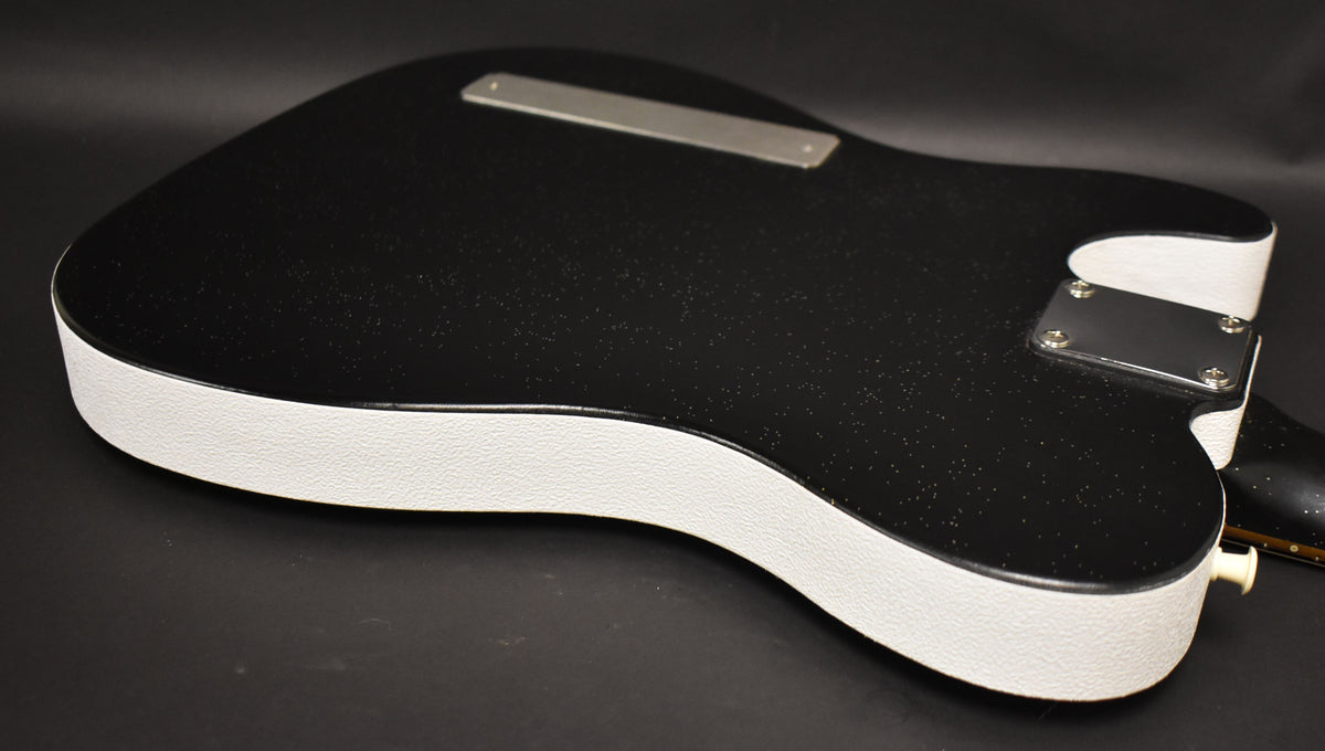 The guitar's black sparkle back and sides are framed, showing a white textured binding and a chrome neck plate.