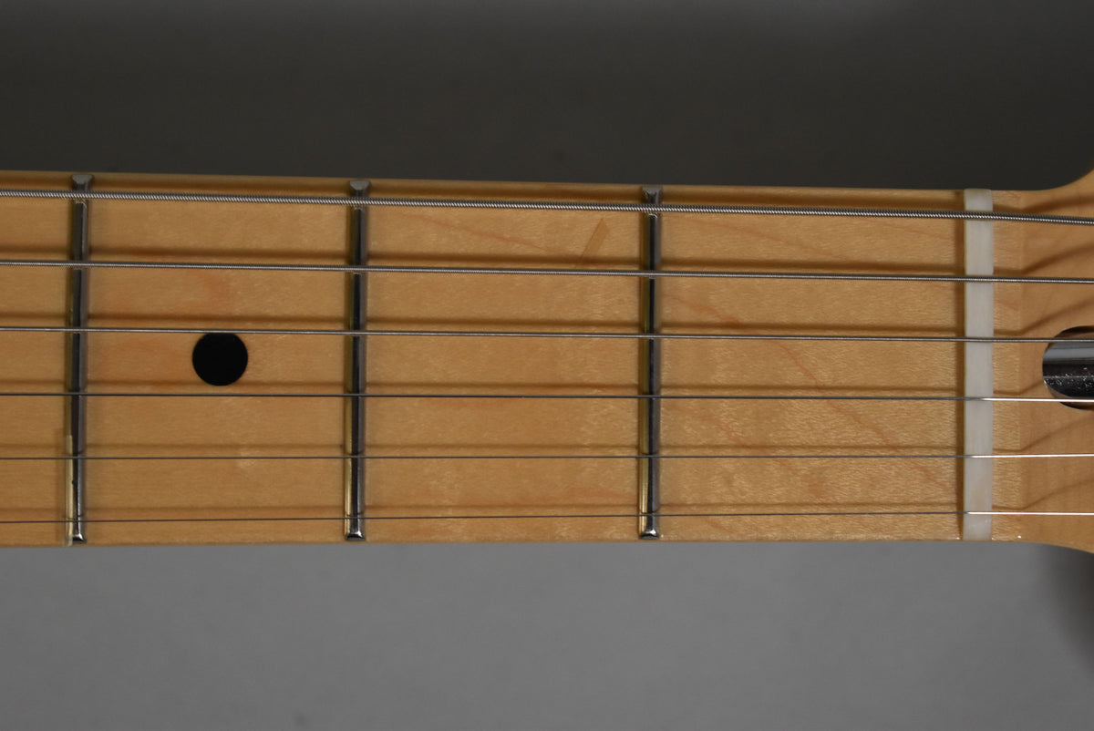 Close-up of the light maple fretboard with a black dot inlay at the 7th fret, silver frets, and a white nut.