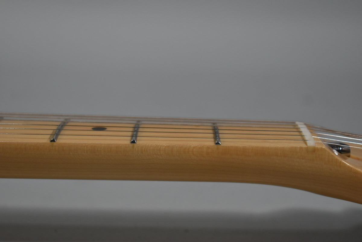 Close-up of the light-colored maple neck and fretboard, showing frets, strings, and a single black dot inlay.