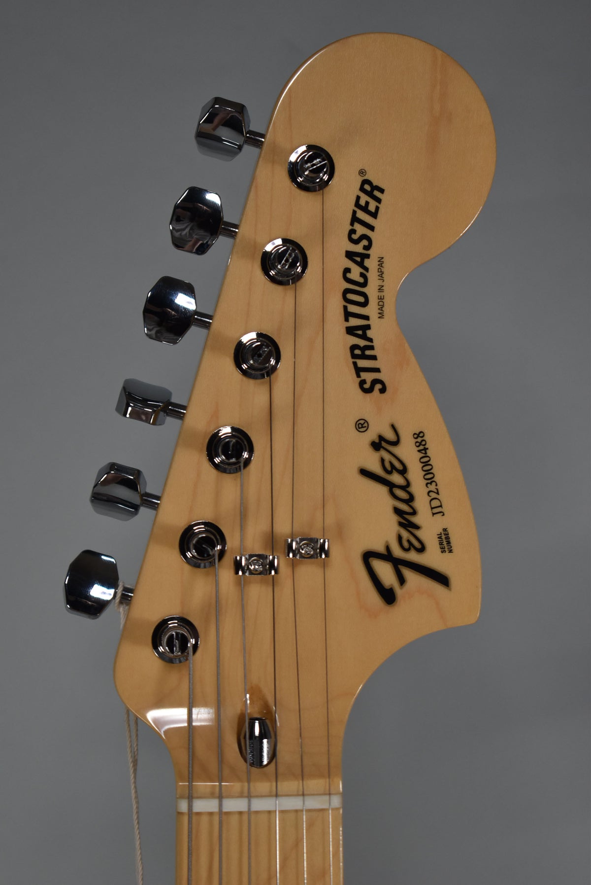 Close-up of a light maple headstock with six chrome tuners, two string trees, and a white nut.