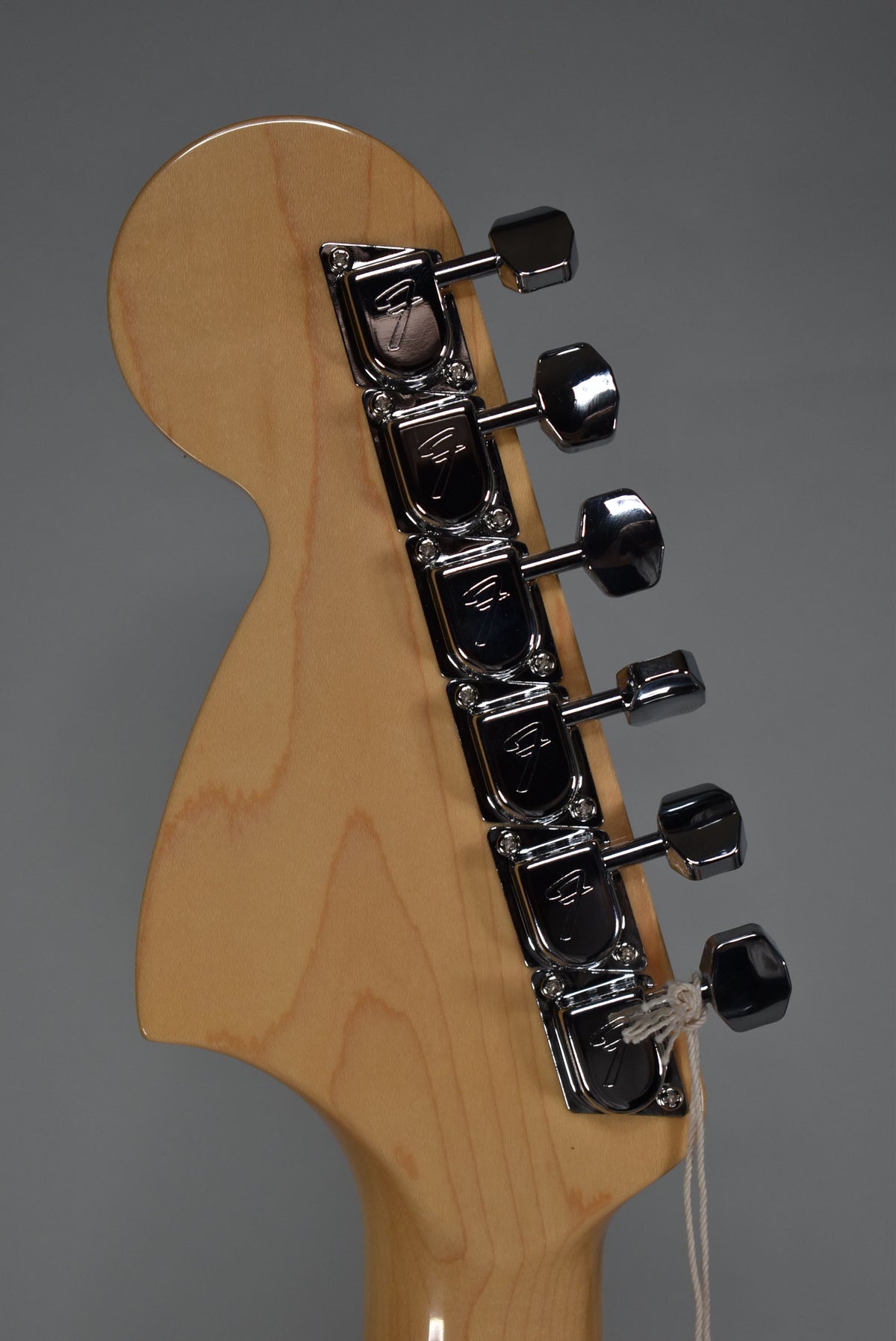 The back of a light wood headstock with six chrome tuners aligned vertically, showing a white string tied to the lowest tuner.